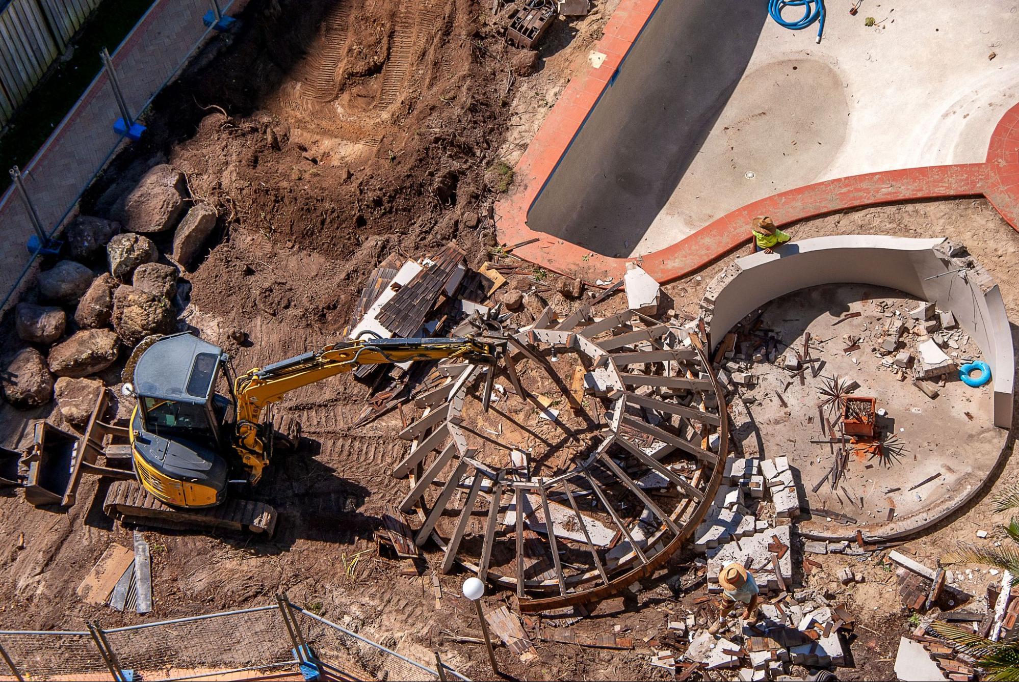 An excavator destroys an old swimming pool on a construction site.