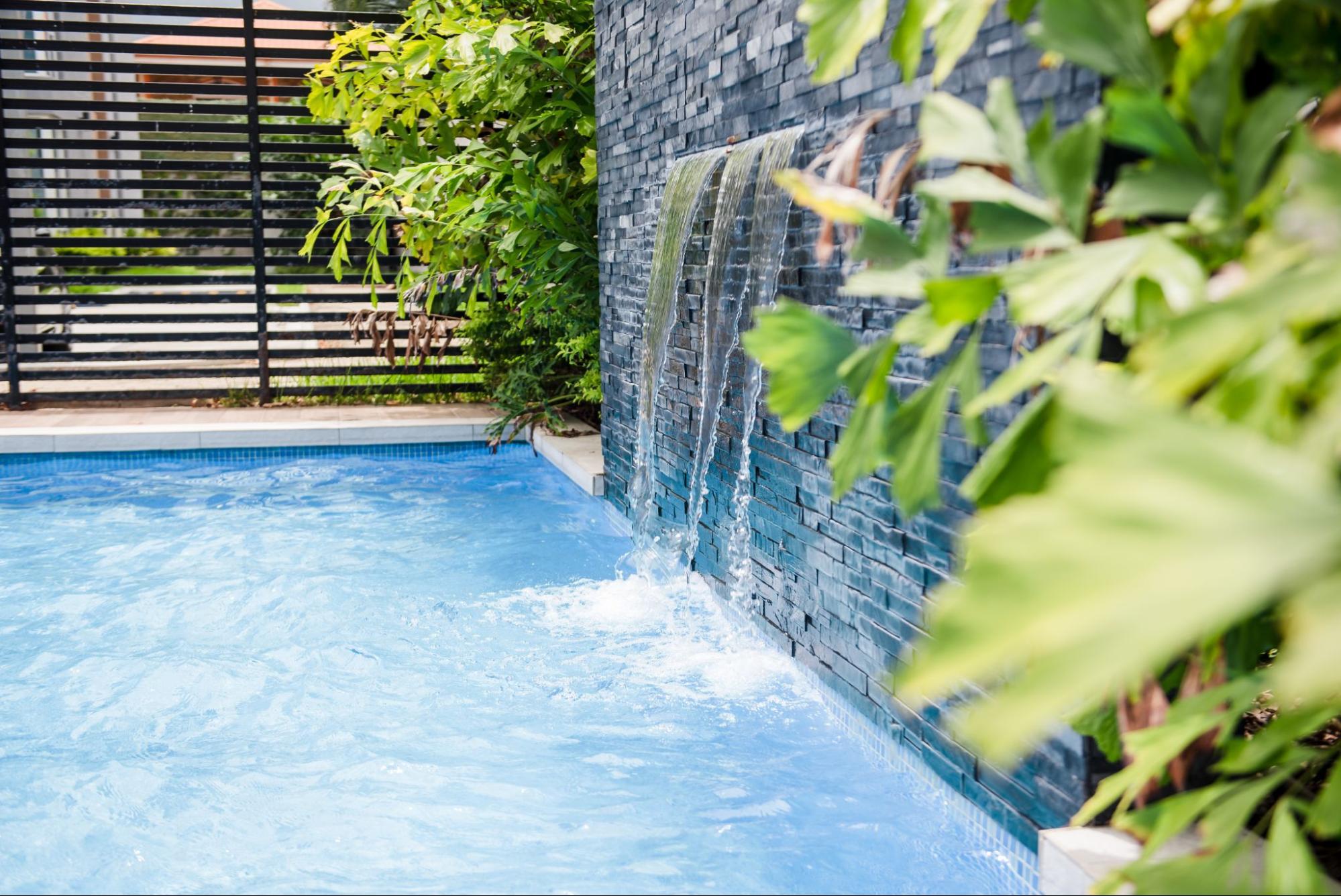 A swimming pool with a waterfall feature and surrounding plants.