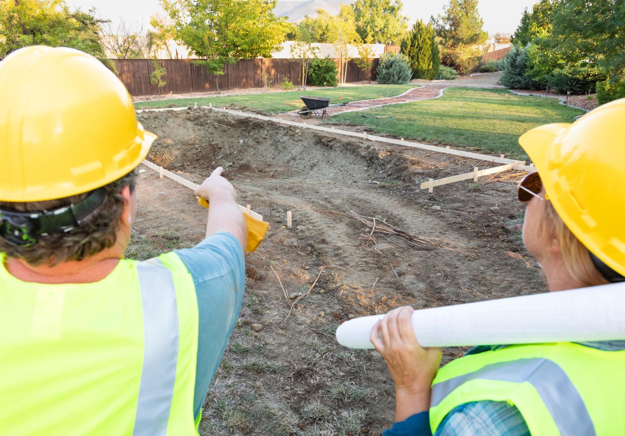 Two workers preparing a backyard construction site.