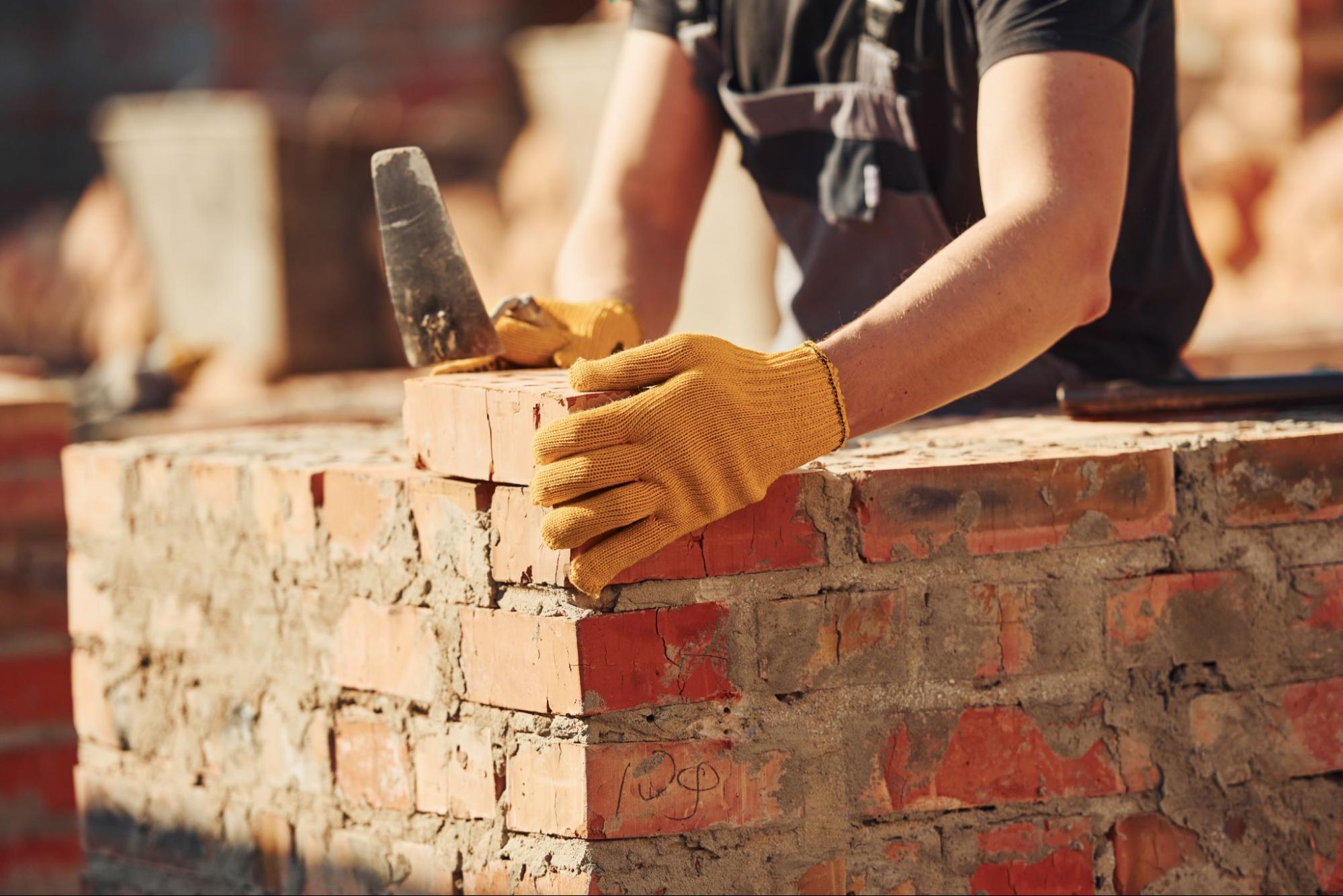 Man in gloves working with cement and bricks.
