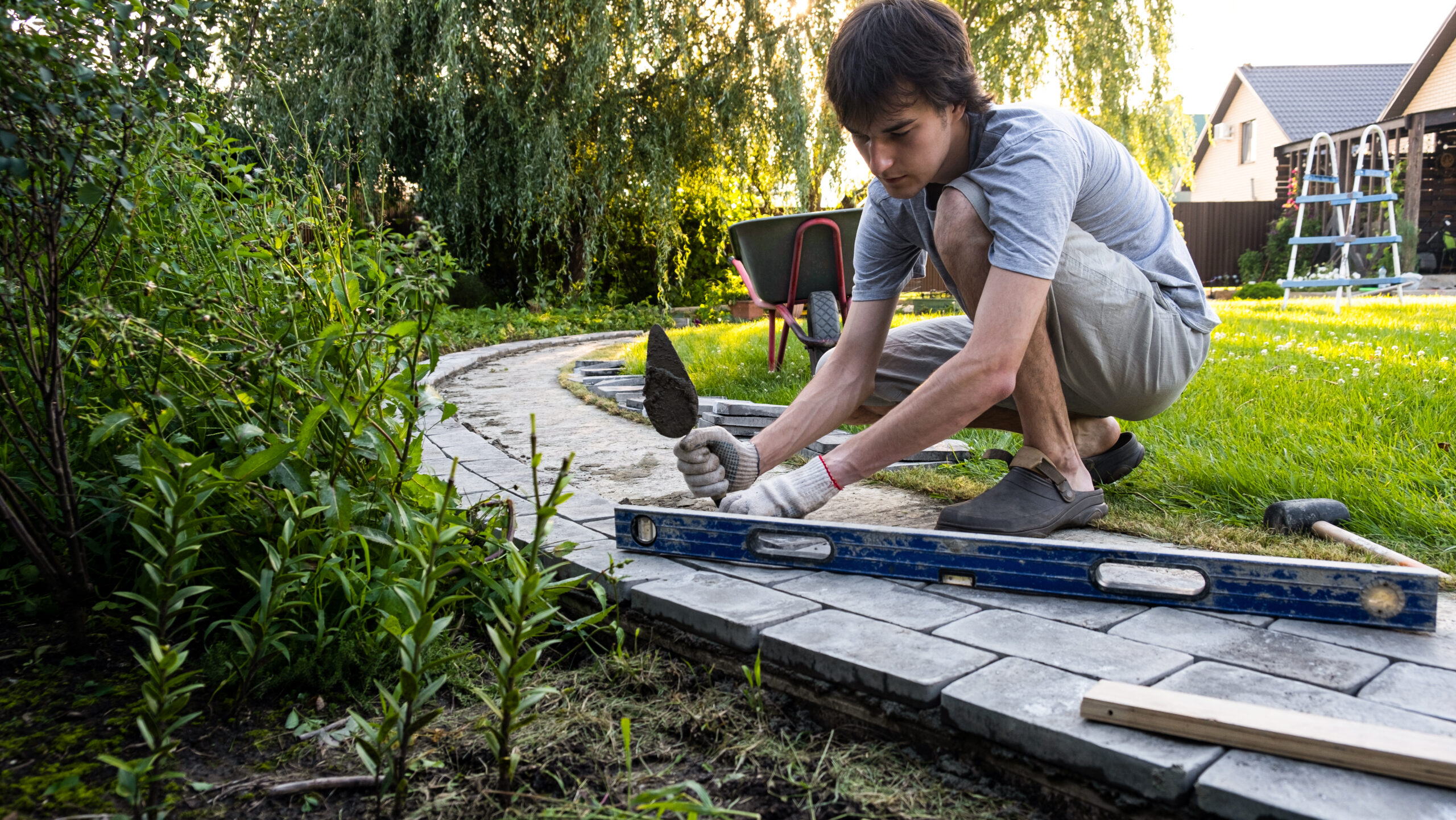 A young man uses a trowel and level to complete a paver install.