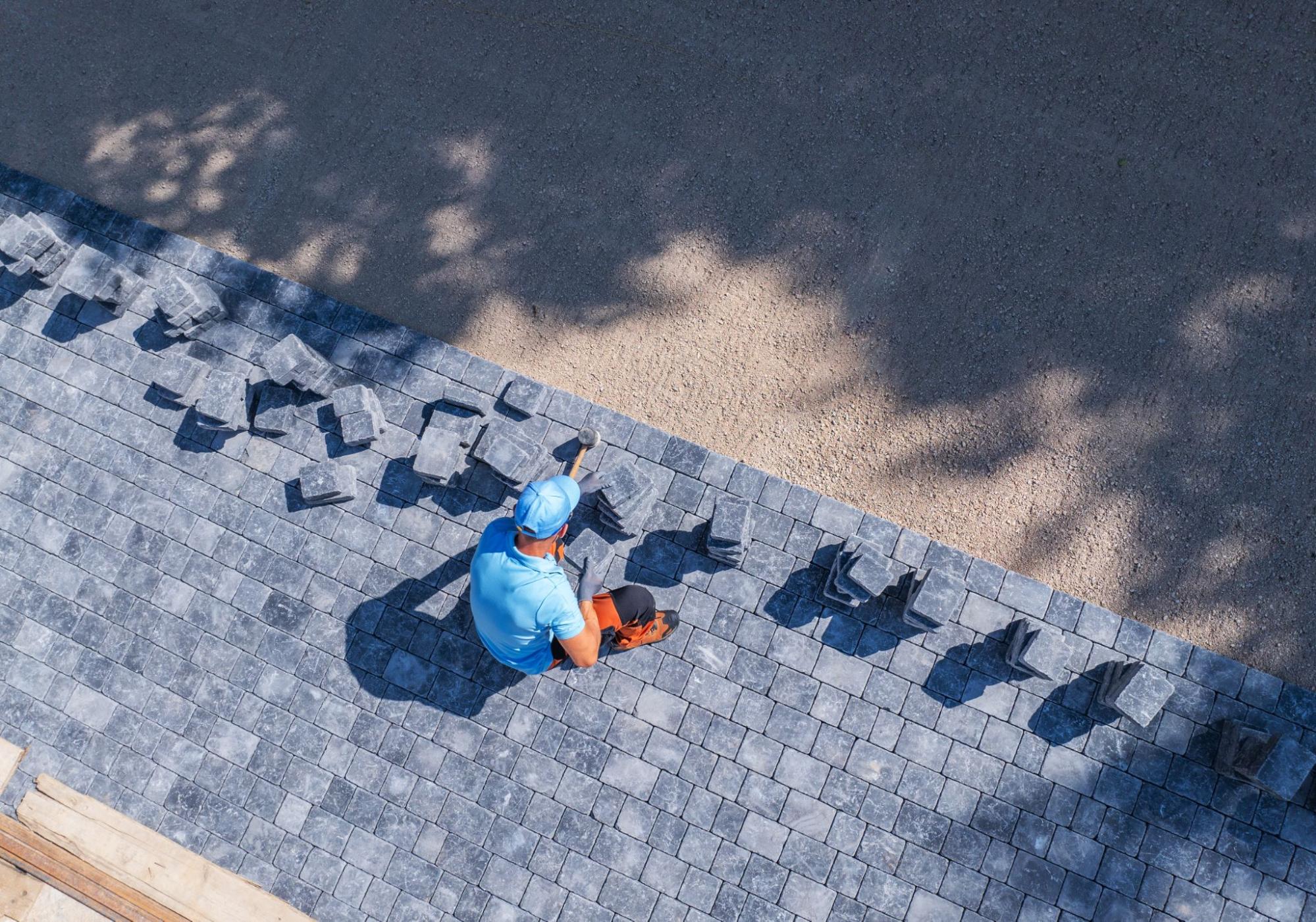 A contractor dressed in blue lays rows of paver stones to build a patio.