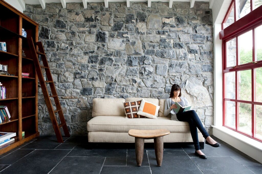 A woman reading on a sofa in a living room featuring a beautifully crafted stonework wall.