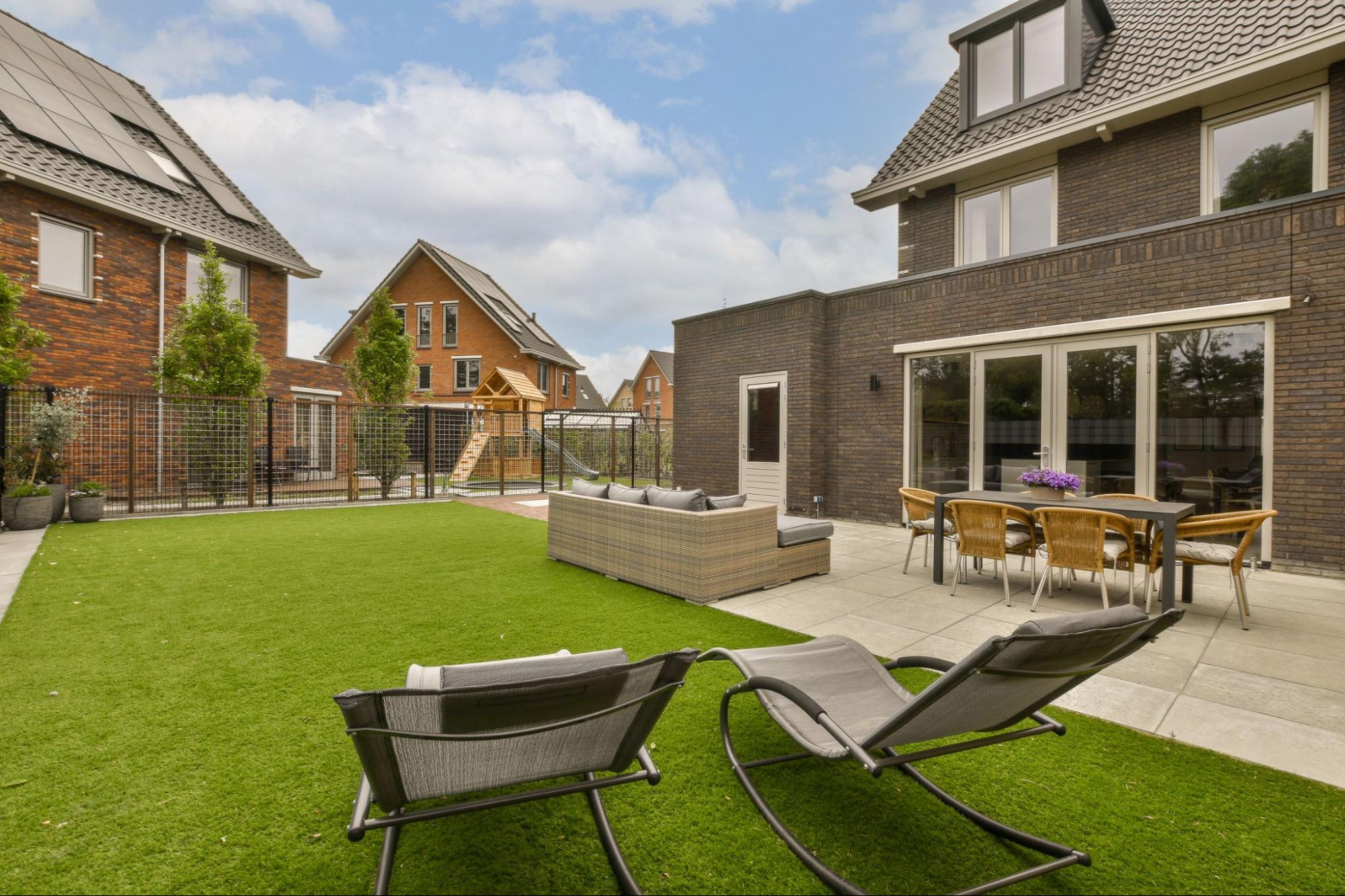 A modern backyard featuring a stylish patio with outdoor chairs surrounded by lush, green artificial turf