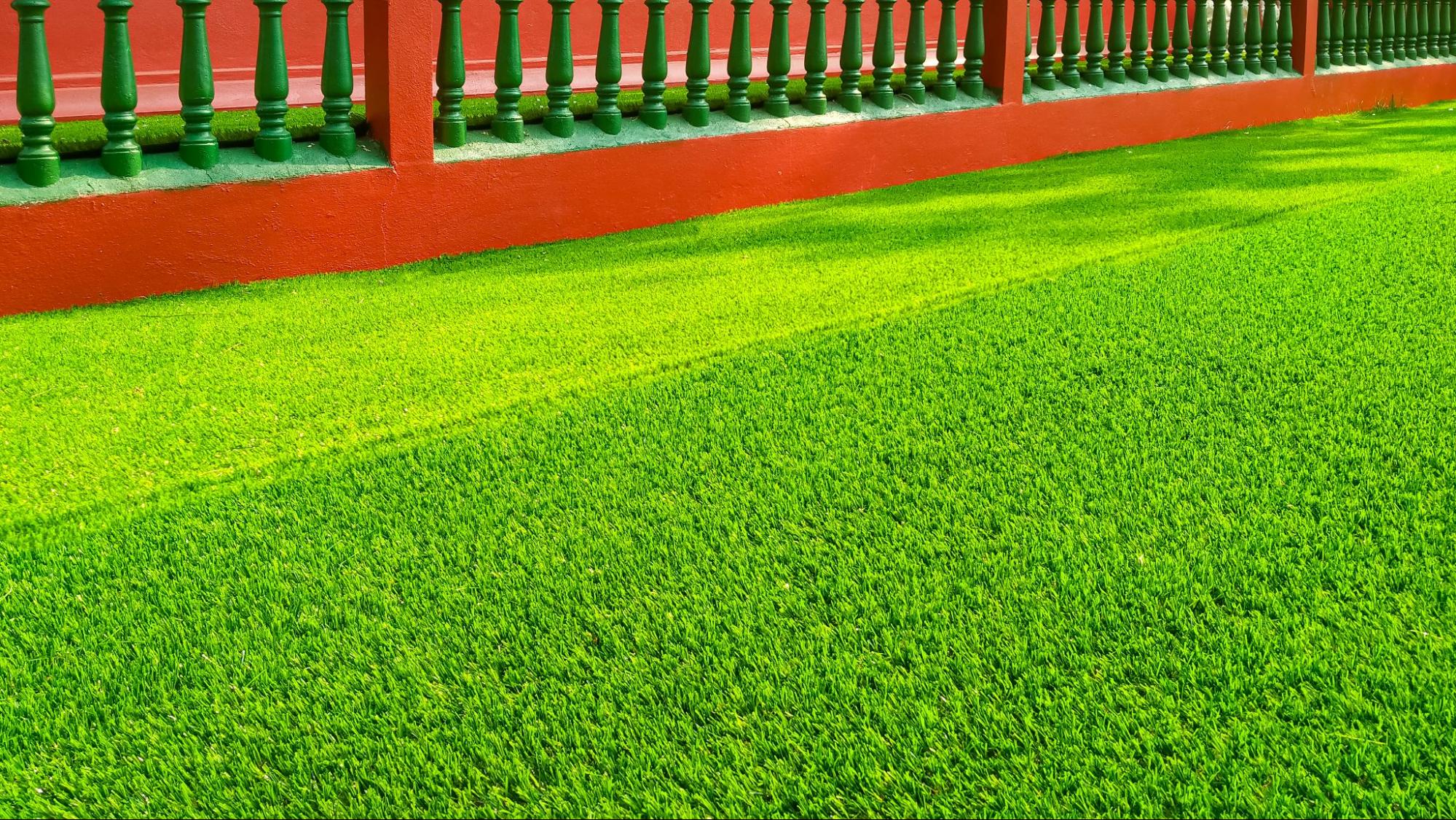 A close-up view of vibrant green artificial turf with red fence balusters in the background