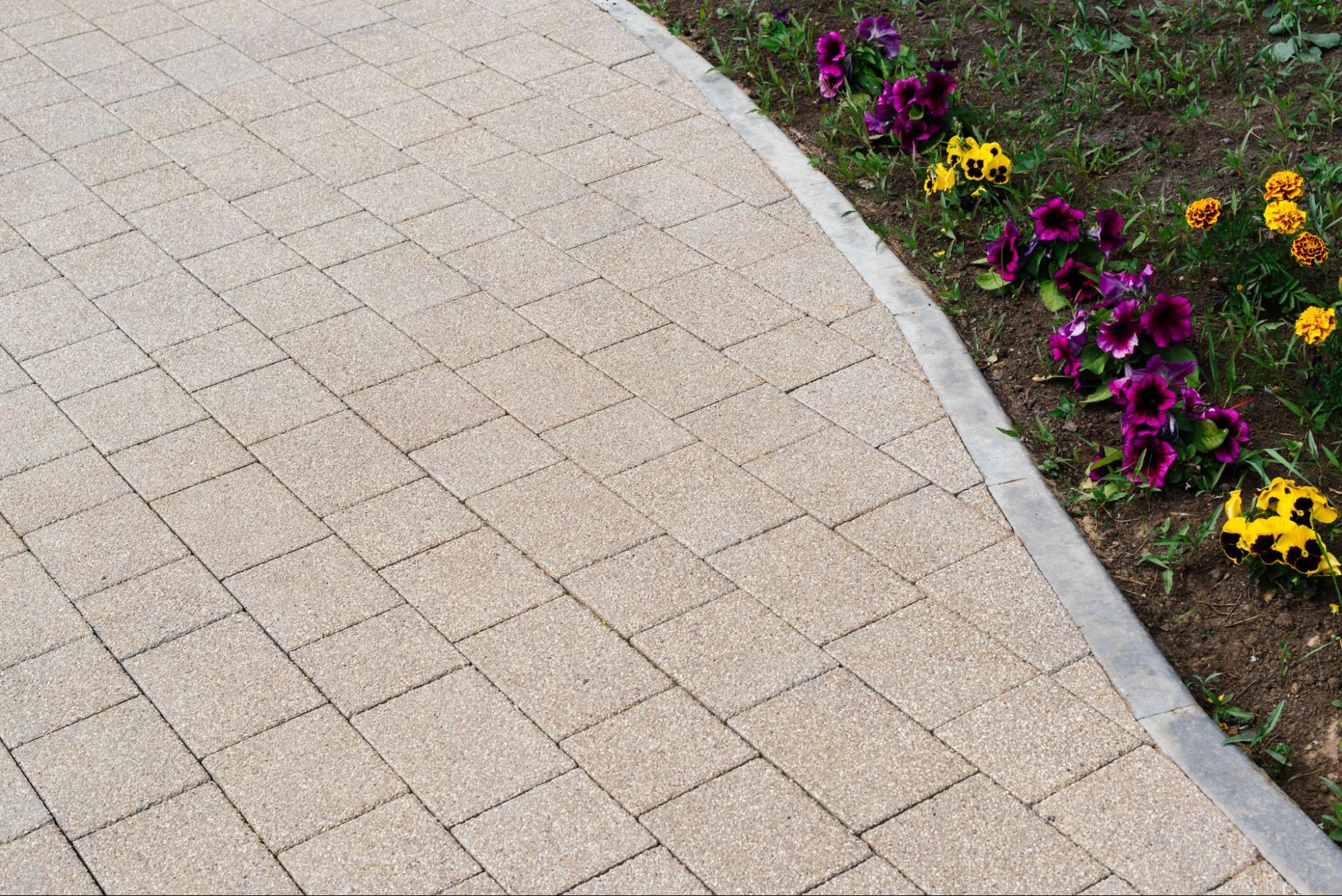 Top and partial view of a paver driveway with a bright, lush flower garden lining one side