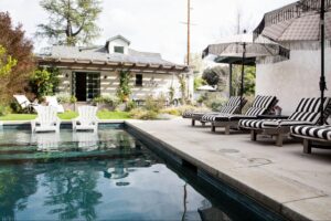 Pool next to lounge chairs, grass, and a home.