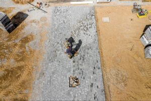 A worker uses a plate compactor to perform a patio installation.